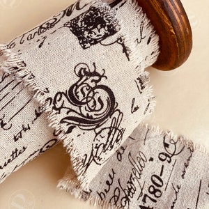 Peut inclure: Gros plan d'une bobine de ruban décoratif. Le ruban est de couleur beige clair avec des écritures et des illustrations noires. Les bords du ruban sont effilochés. La bobine est en bois et a une finition marron foncé.