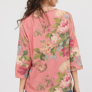 Puede incluir: Una blusa rosa con mangas tres cuartos y un estampado floral. El dise&ntilde;o presenta grandes flores coloridas en tonos rosa, crema y burdeos, con hojas verdes. La blusa est&aacute; hecha de un material suave y tiene un corte holgado.