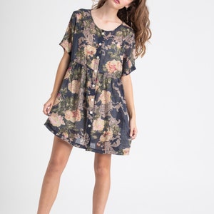 Puede incluir: Un vestido de manga corta con botones y estampado floral en tonos rosa, verde y crema sobre un fondo azul marino.