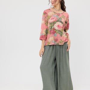 Puede incluir: Conjunto femenino con una blusa rosa con estampado floral y mangas tres cuartos, y pantalones de pierna ancha verde oliva. La blusa tiene cuello redondo y los pantalones tienen un corte holgado y fluido. El conjunto est&aacute; sobre un fondo blanco.