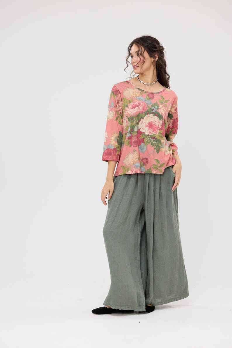 Puede incluir: Conjunto femenino con una blusa rosa con estampado floral y mangas tres cuartos, y pantalones de pierna ancha verde oliva. La blusa tiene cuello redondo y los pantalones tienen un corte holgado y fluido. El conjunto est&aacute; sobre un fondo blanco.
