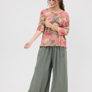 Puede incluir: Conjunto femenino con una blusa rosa con estampado floral y mangas tres cuartos, y pantalones de pernera ancha verde oliva. La blusa tiene cuello redondo. Los pantalones son holgados. El conjunto se completa con bailarinas negras.