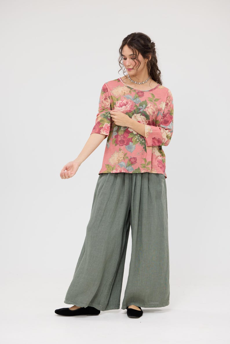 Puede incluir: Conjunto femenino con una blusa rosa con estampado floral y mangas tres cuartos, y pantalones de pernera ancha verde oliva. La blusa tiene cuello redondo. Los pantalones son holgados. El conjunto se completa con bailarinas negras.