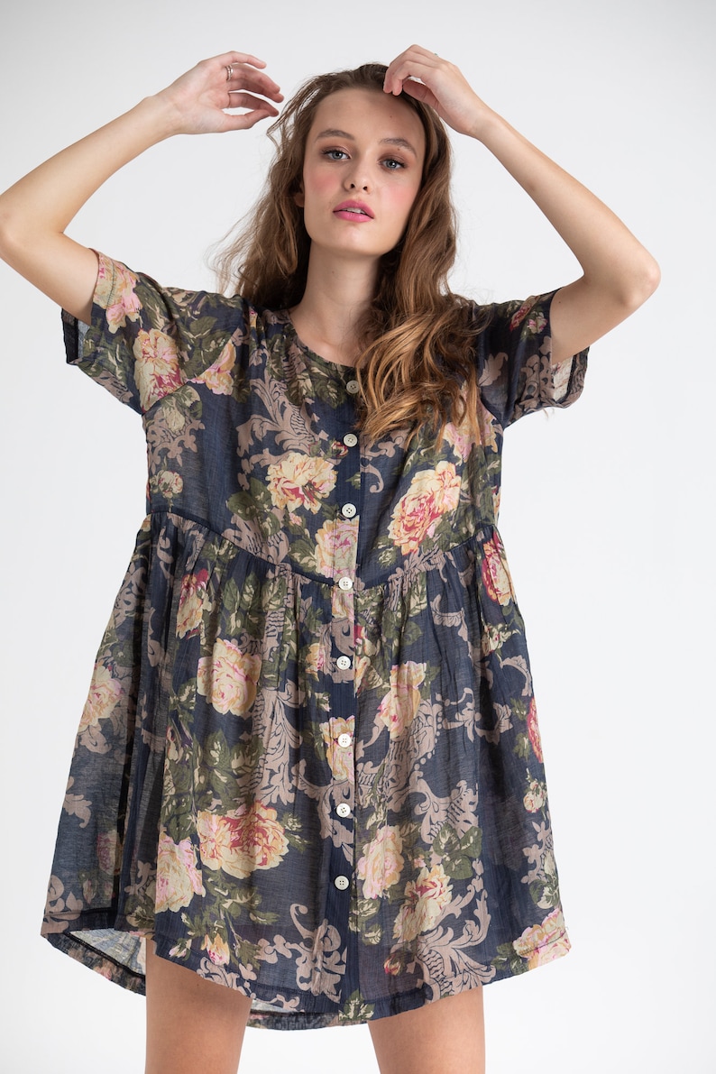 Puede incluir: Un vestido de estampado floral azul marino con mangas cortas y botones en la parte delantera. El vestido tiene una falda fruncida y un corte holgado.