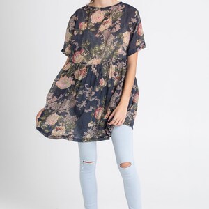 Puede incluir: Una mujer lleva un vestido de estampado floral azul oscuro de corte holgado y mangas cortas. Tambi&eacute;n lleva unos vaqueros azules claros con las rodillas desgastadas.