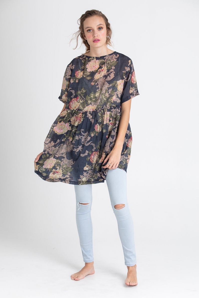 Puede incluir: Una mujer lleva un vestido de estampado floral azul oscuro de corte holgado y mangas cortas. Tambi&eacute;n lleva unos vaqueros azules claros con las rodillas desgastadas.