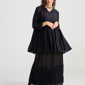 May include: A black two-piece outfit consisting of a long-sleeved top and a maxi skirt. The top has a flared silhouette, and the skirt features a detailed, scalloped hem. The outfit is paired with black Mary Jane shoes.