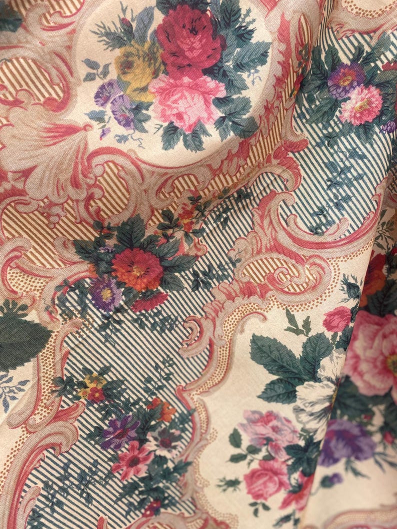 Puede incluir: Una tela con un patr&oacute;n repetitivo de ramos de flores rosas, rojas y moradas encerrados en marcos de volutas ornamentales claras. El fondo consiste en finas rayas verticales oscuras sobre una base de color crema.