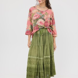 Puede incluir: Conjunto femenino con una blusa rosa con estampado floral y mangas tres cuartos, y una falda larga verde oliva con volantes y borde de encaje. El conjunto se completa con bailarinas rosas claras.