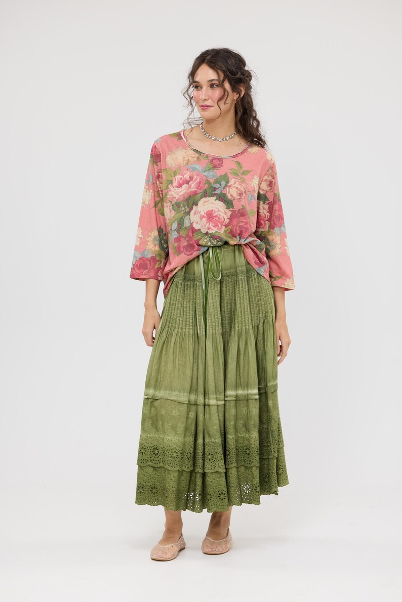 Puede incluir: Conjunto femenino con una blusa rosa con estampado floral y mangas tres cuartos, y una falda larga verde oliva con volantes y borde de encaje. El conjunto se completa con bailarinas rosas claras.