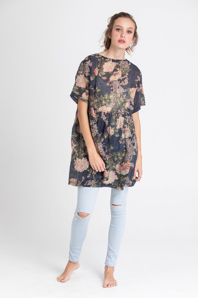 Puede incluir: Un vestido de estampado floral azul marino con mangas cortas y cintura fruncida. El vestido se lleva con jeans azul claro.