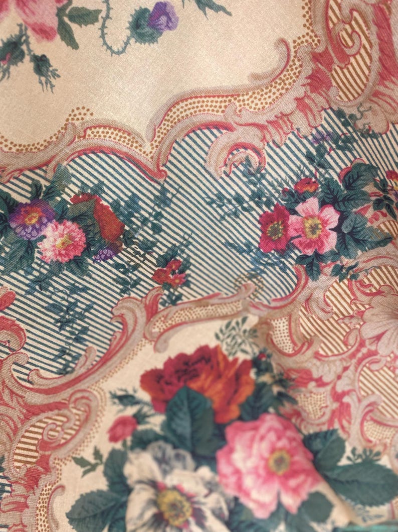 Puede incluir: Una tela con un patr&oacute;n floral de flores rosas, rojas y moradas sobre un fondo crema. El dise&ntilde;o incluye bordes intrincados de volutas en un tono rojo apagado y secciones de finas rayas verticales de color azul oscuro sobre fondo crema.
