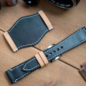 May include: Black leather watch strap with white stitching and a tan leather lining. The strap is shown with a separate tan leather watch strap keeper.