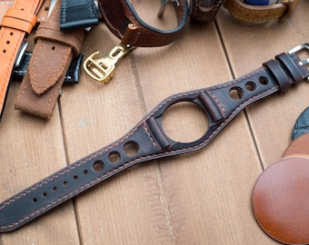 May include: A dark brown leather watch strap with stitching and holes for ventilation. The strap has a unique design with a cutout for the watch face.