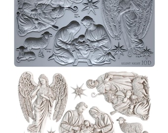 May include: A gray silicone mold featuring recessed designs of a nativity scene, including a central family, an angel with wings, sheep, and stars. The mold includes printed text 'SILENT NIGHT IOD' and various volume and weight measurements in ml and g.