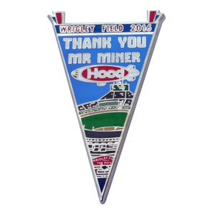 May include: A silver metal pin shaped like a pennant with a blue background and a white outline. The pin features a baseball stadium with a blimp that says "Hood's" in red letters. The text on the pin reads "Wrigley Field 2016 Thank You Mr. Miner".
