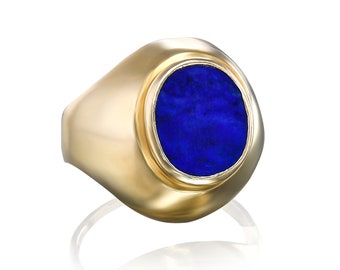 Op de afbeelding: Een gouden ring met een grote, ovale blauwe edelsteen in een bezel-setting.