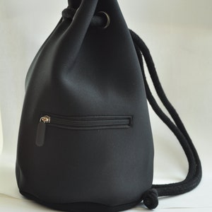 May include: A black drawstring backpack with a zipped pocket on the front. The bag is made from a water-resistant material and has a long, adjustable strap.