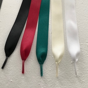 May include: Five different coloured ribbon shoelaces. The shoelaces are black, red, green, cream, and white.