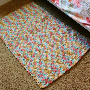 Puede incluir: Una alfombra de crochet con un patr&oacute;n de chevron en tonos de rosa, azul y beige.