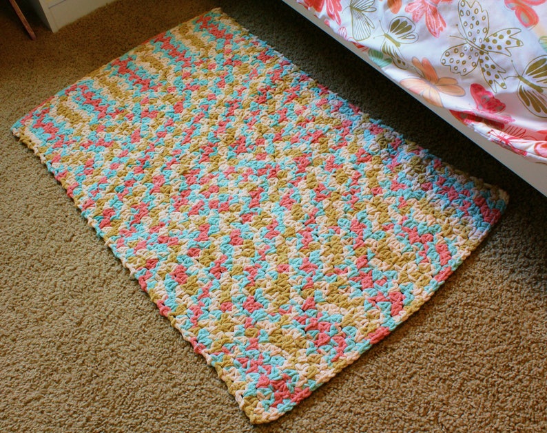 Puede incluir: Una alfombra de crochet con un patr&oacute;n de chevron en tonos de rosa, azul y beige.