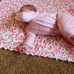 Puede incluir: Una manta de beb&eacute; de crochet rosa y blanca con un beb&eacute; acostado encima.