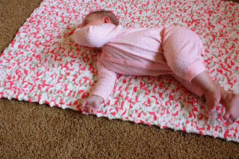 Puede incluir: Una manta de beb&eacute; de crochet rosa y blanca con un beb&eacute; acostado encima.
