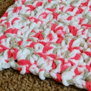 Puede incluir: Primer plano de una manta de ganchillo con un patr&oacute;n de color rosa, blanco y beige.