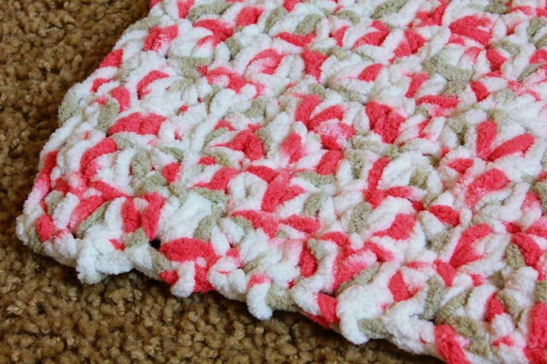 Puede incluir: Primer plano de una manta de ganchillo con un patr&oacute;n de color rosa, blanco y beige.