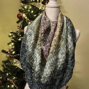 Peut inclure: Une écharpe infinie en crochet dans des tons de bleu, vert et violet. L'écharpe est réalisée avec un point texturé et présente un dégradé de couleurs.