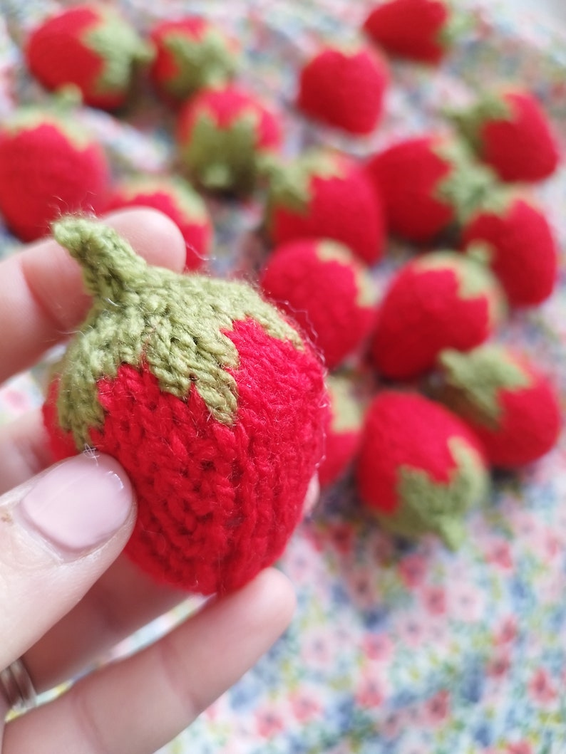 May include: A collection of knitted strawberries in red and green. The strawberries are made of yarn and have a realistic appearance.
