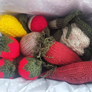 May include: A collection of knitted fruit and vegetables, including a yellow lemon, a red strawberry, a green pepper, and a red carrot.