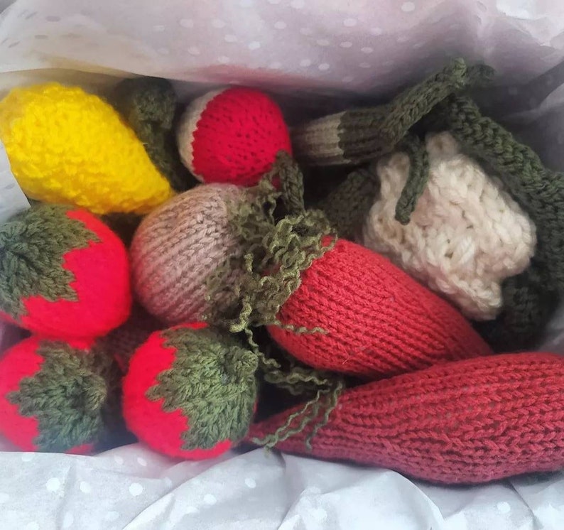 May include: A collection of knitted fruit and vegetables, including a yellow lemon, a red strawberry, a green pepper, and a red carrot.