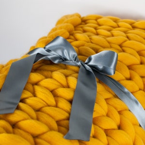 May include: A large, chunky knit throw blanket in a bright yellow color. The blanket is tied with a gray satin ribbon.