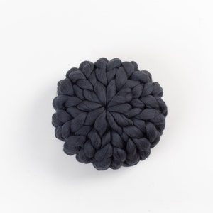 May include: A dark gray round knitted pillow with a unique braided design.