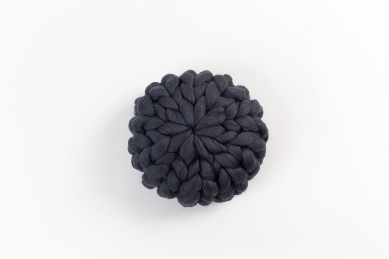 May include: A dark gray round knitted pillow with a unique braided design.