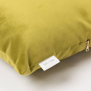 May include: A mustard yellow velvet pillow with a zipper closure and a white label that says "CUP + TEA".
