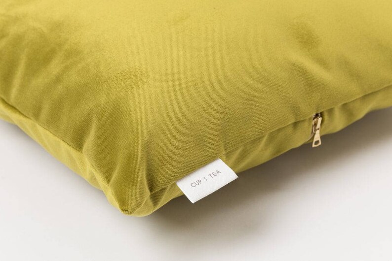 May include: A mustard yellow velvet pillow with a zipper closure and a white label that says "CUP + TEA".