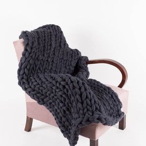 May include: A dark gray chunky knit throw blanket draped over a pink armchair with wooden arms and legs.