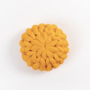 May include: A round, yellow knitted pillow with a chunky knit texture.