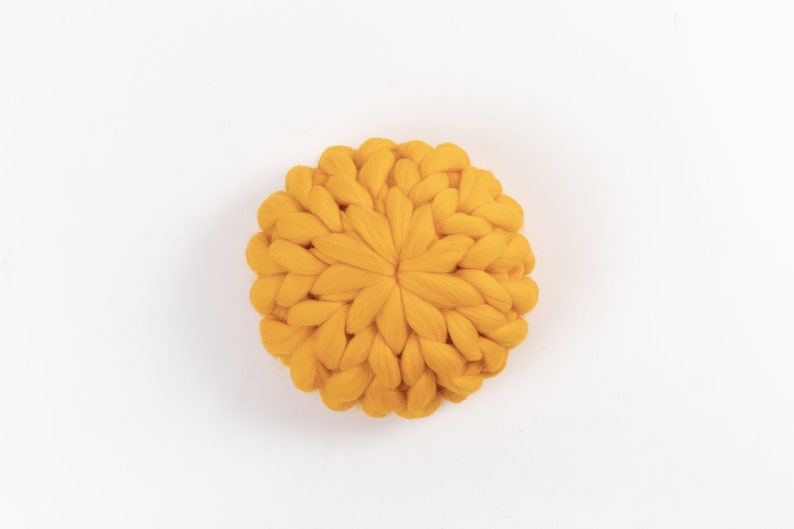 May include: A round, yellow knitted pillow with a chunky knit texture.