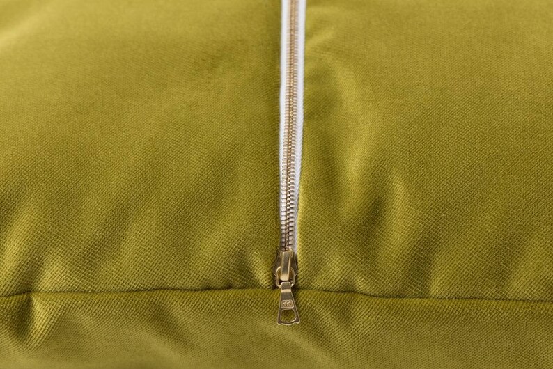 May include: A close-up of a green velvet pillow with a gold zipper. The zipper is open and the fabric is soft and plush.