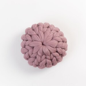 May include: A round, mauve-colored knitted pillow with a textured, woven design.