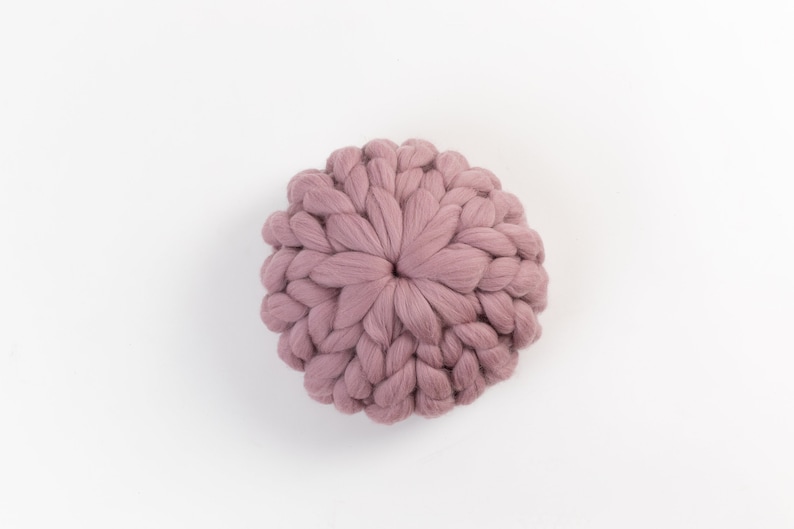 May include: A round, mauve-colored knitted pillow with a textured, woven design.