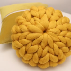 May include: A large, round, yellow knitted throw pillow. The pillow is made of thick, chunky yarn and has a soft, fluffy texture.