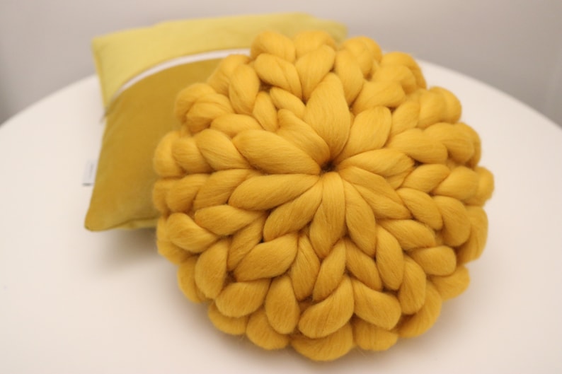 May include: A large, round, yellow knitted throw pillow. The pillow is made of thick, chunky yarn and has a soft, fluffy texture.