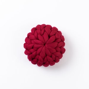Puede incluir: Un coj&iacute;n redondo de punto rojo con un dise&ntilde;o trenzado &uacute;nico.