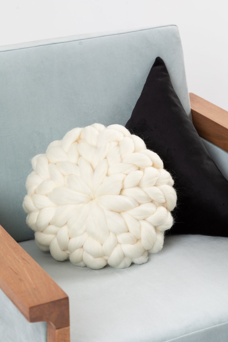 May include: A white chunky knit throw pillow on a light blue armchair with a black pillow behind it.