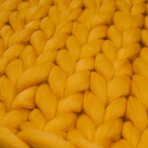 May include: A close-up of a yellow knitted blanket with a chunky knit texture.