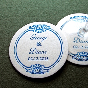 May include: Two round white coasters with blue decorative borders and the text "George & Diane 02.12.2015" on each.
